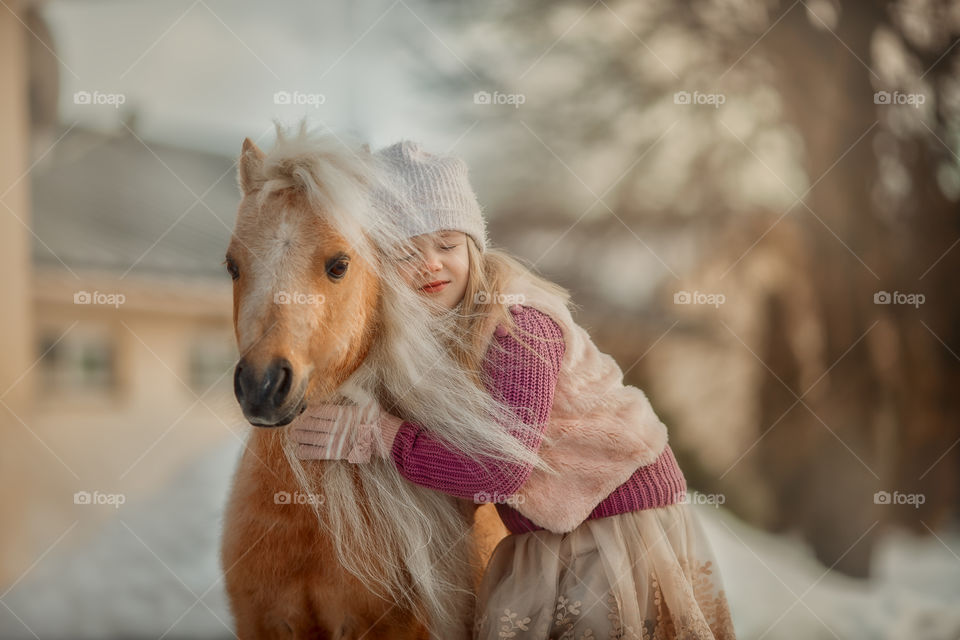 Little girl with palomino pony at winter sunny day