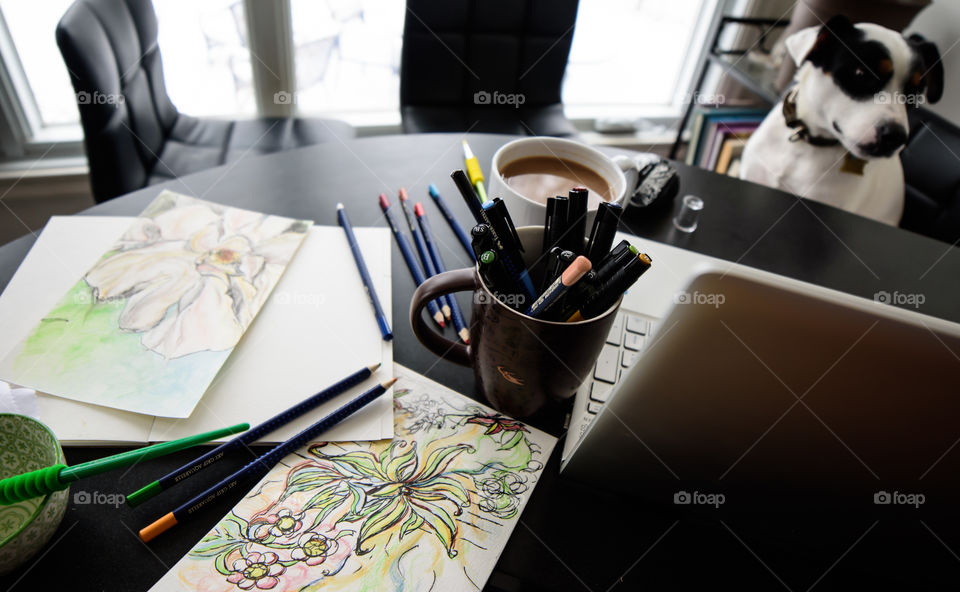 Cute dog at table near window with Faber-Castell artist supplies, sketchbooks, floral sketches and coffee next to laptop and sketches with Aquarelle pencils and PiTT artist pens lifestyle and creativity background