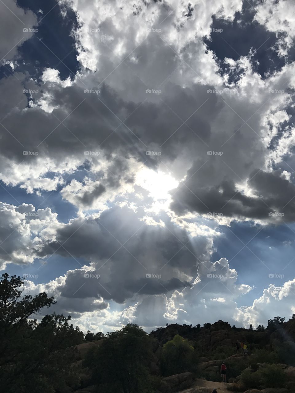 Dramatic sky in Prescott, Arizona. Deep, vivid blue sky broken up by clouds with an intense, glaring sun peeking through. 