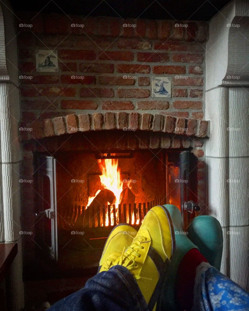 Two pair of feet of a couple cosy sitting in a couch in front of the Burning fireplace 