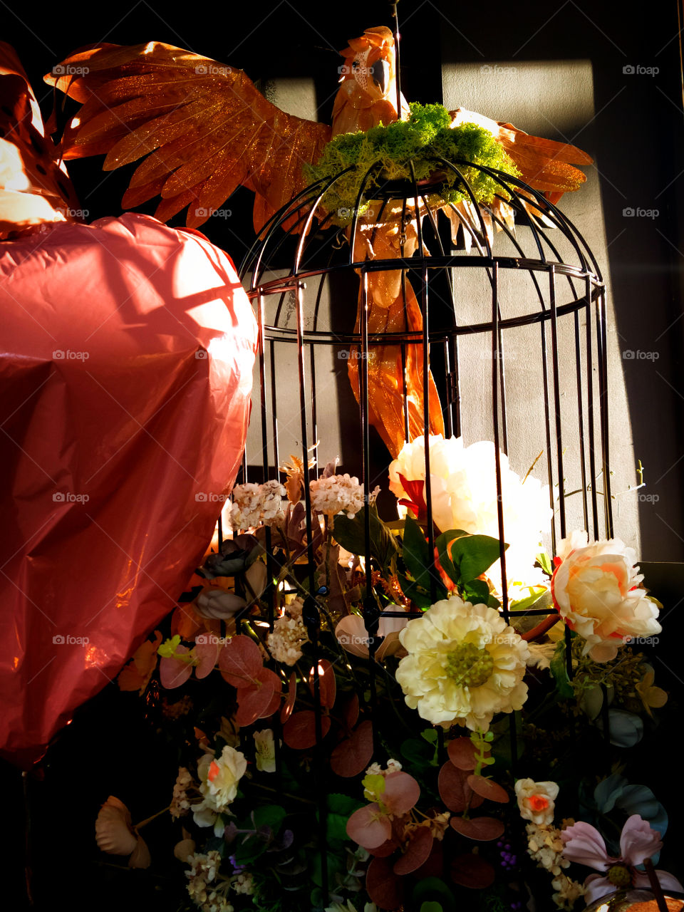 Bird cage, which is decorated with a decorative bouquet of artificial flowers.  Top of the cage is a toy parrot