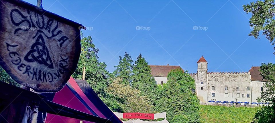 A picturesque view of “Ortenburg” in “Bavaria”, Germany near the Austrian border. As part of this year’s “Renaissance Festival” in the foreground a wooden sign for “Lederhandwerk” or leather craftsmanship is being displayed. 2023. Hypnotic Production