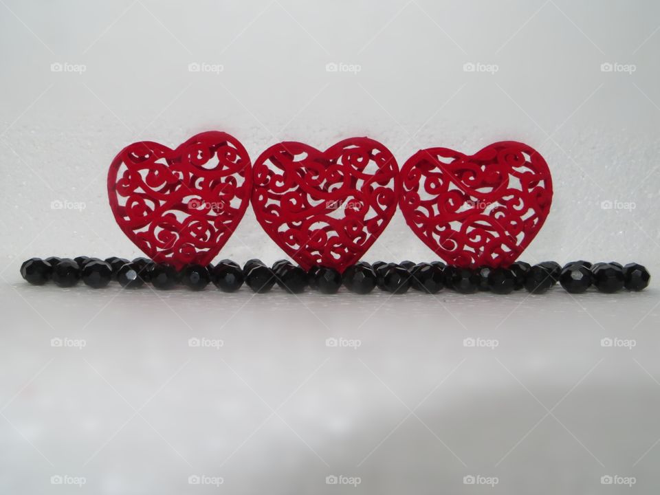 On a white background there are three red hearts and black beads made of agate stone. Love, postcard, silence