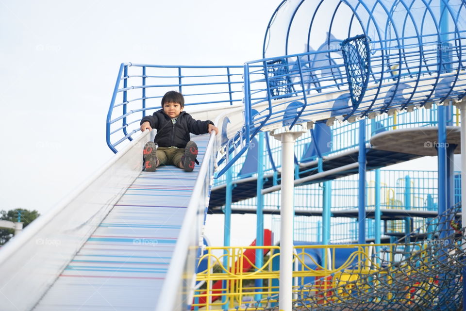 Asian boy sliding down playground slide