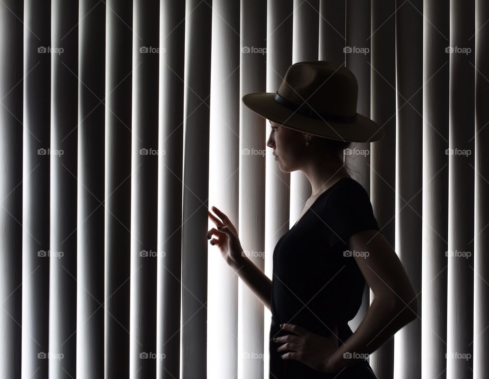 Silhouette of a beautiful woman looking through the window blinds 