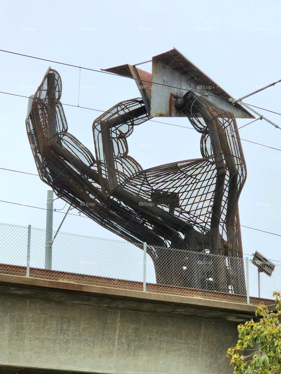 A giant metal hand statue throws a large "paper" airplane composed of metal at a location near a major airport