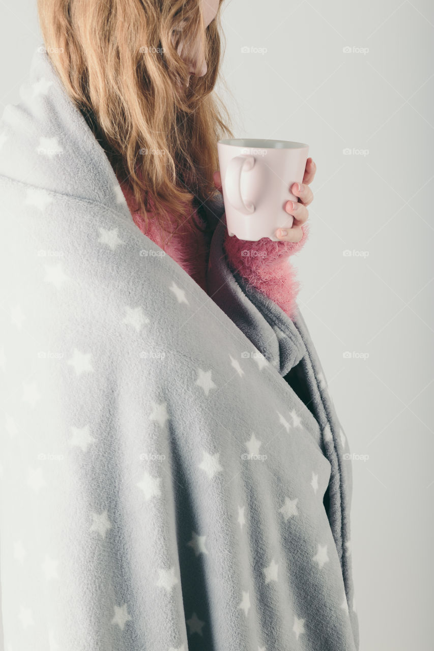 Young woman has caught cold, has day off, sick day, wrapped in blanket, holds cup of herbal tea. Profile portrait view