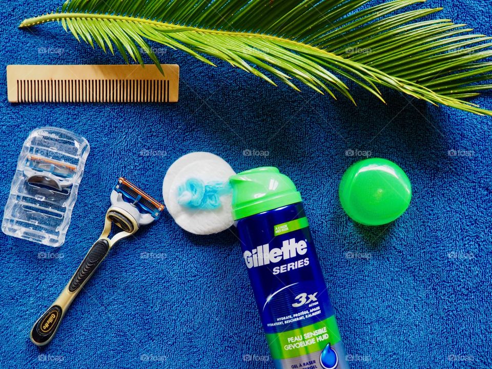 Gillette shaving cream and razor on a blue towel with comb and palm leaf.