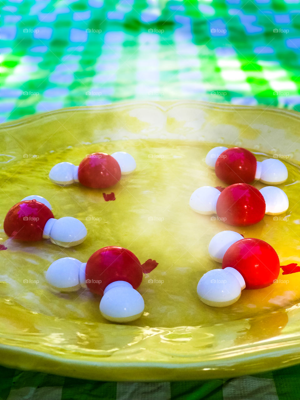 Clash of Colours: Red (Hydrogen) & white (Oxygen) single molecule models of gaseous H2O(water) in a pool of boiling water. The H2O molecules repel each other forming steam/vapour to rise off the yellow plate which rests on a green plaid tablecloth. 🌫