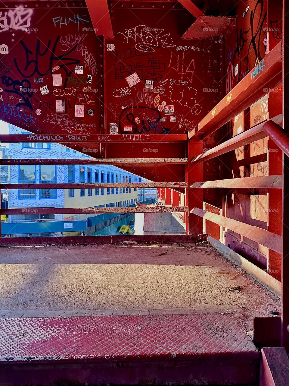 This is the middle platform of the red metal staircase of the “Pulaski Bridge” at “Newtown Creek” in “Greenpoint”, Brooklyn with the bright golden light of the setting sun shining in. 2024. Hypnotic Productions
