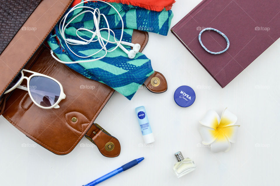Contents of summer bag laid out on a white table with items consisting of Nivea cream, Nivea lip care, sunglasses, ear buds, book, hair tie, pen and fragrance