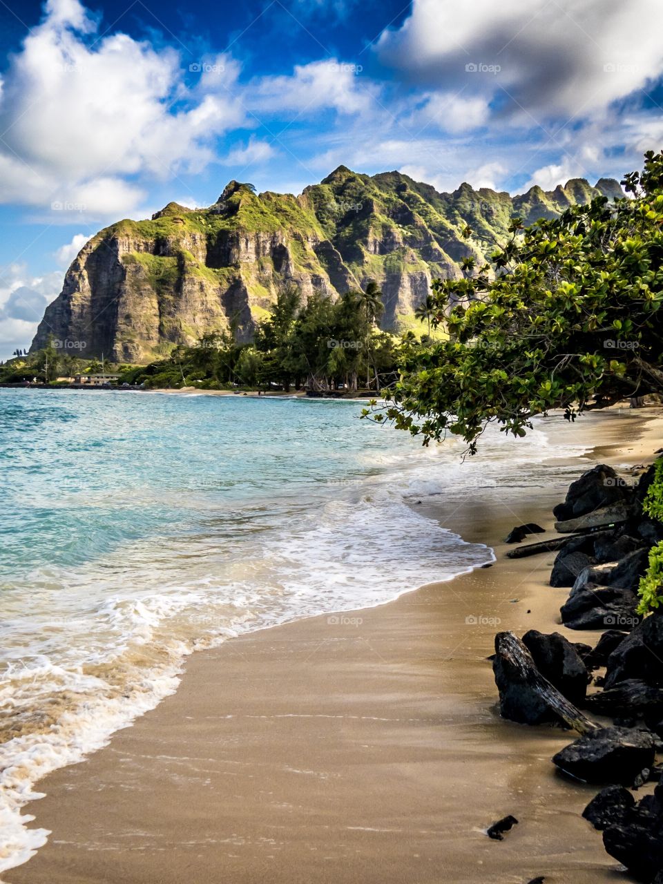 A beach on the windward side of Oahu, Hawaii where the Pacific Ocean meets the Jurassic looking mountains of the island. 
