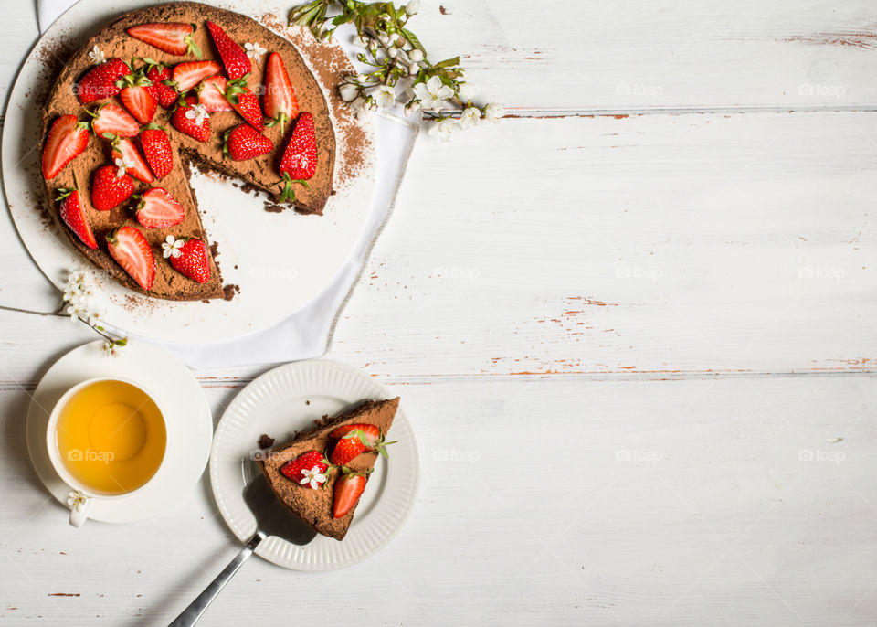 Vegan chocolate cake decorated with fresh strawberries on a white wooden table. 