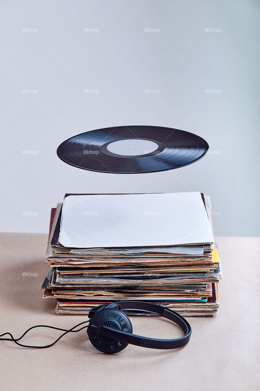 Black vinyl hung in the air over stack of many black vinyl records, headphones put at the front of vinyls. Copy space for text. Candid people, real moments, authentic situations