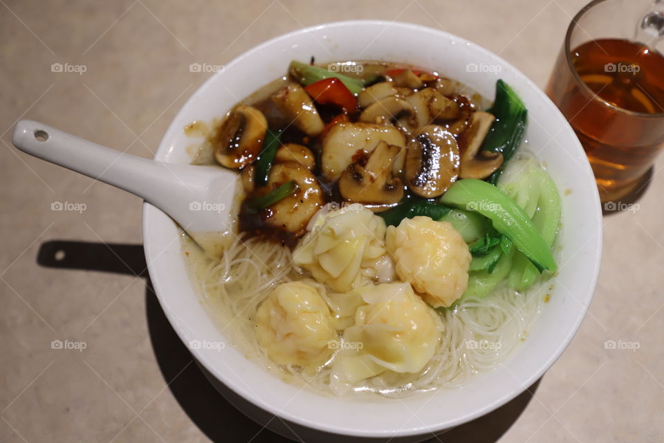 Bowl of noodle soup with mushrooms and wontons on a tabletop 