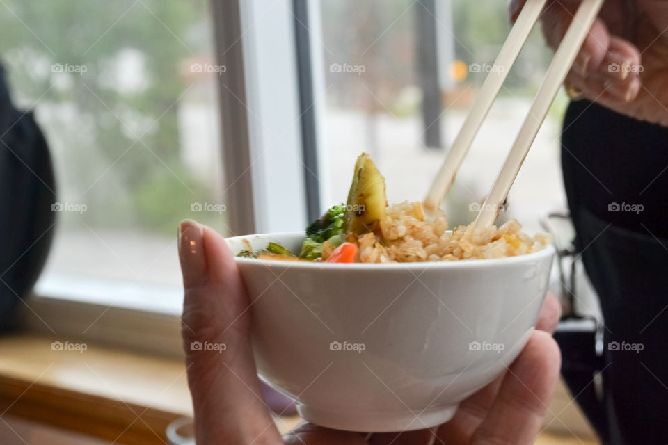 Woman's hand holding bowl of Asian food and chopsticks, woman eating 