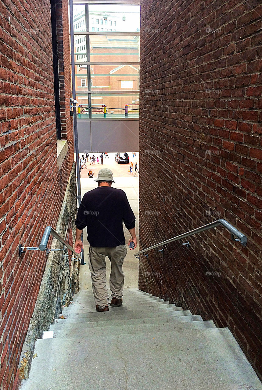 Old man walks down the stairs between two brick buildings. Providence, USA