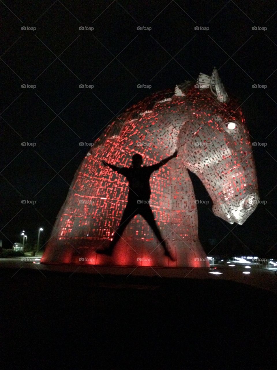 Silhouette of my son son jumping in the air in front of  one of The Kelpies lit up in red against the black sky.