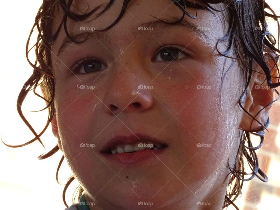 closeup of a boys face dripping wet after playing with water on a summers day