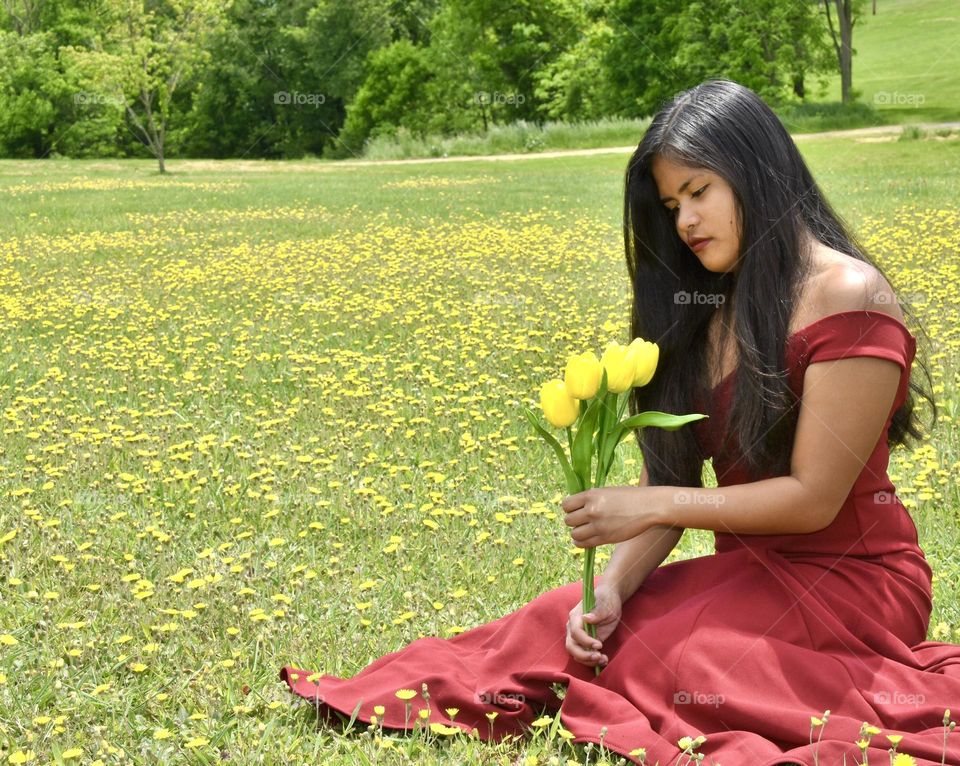 A girl sitting in a field of buttercups and holding yellow daffodils