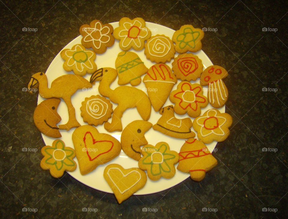 Various Shaped Iced Biscuits / Cookies Decorated With Writing Icing - Ice Creams , Bells , Stars , Hearts , Moons , Flowers , Rocking Horse , Mushrooms , Flamingo Shapes Cookie Cutters Selection On A White Plate