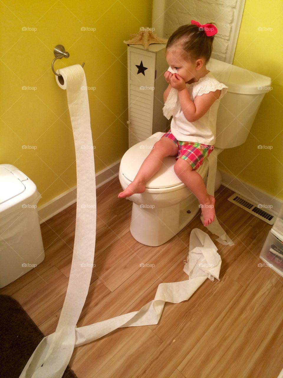 Little girl sitting on toilet bowl with tissue