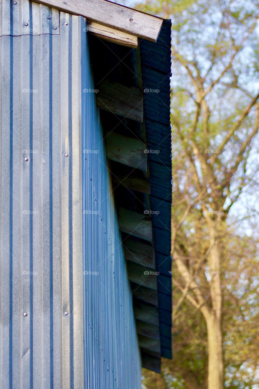 Metal Shed Overhang - metal shed siding showing bluish in the early morning light, wooden overhang beams seen at an angle, rural setting