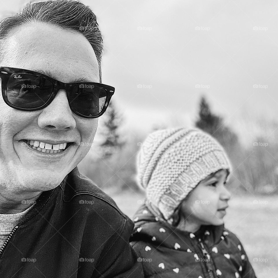 Black and white portrait of man and toddler girl, toddler girl looks off into the distance while man smiles, portrait photography with a smartphone, monochrome portrait image, album cover portrait, black and white people photograph