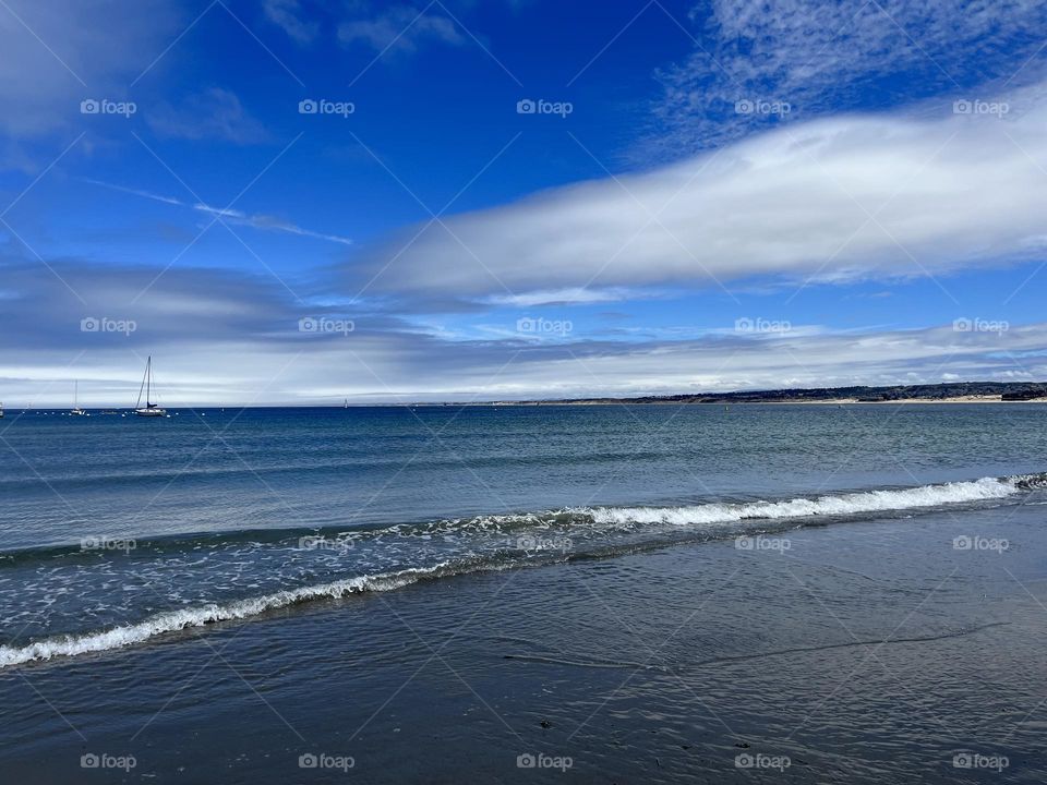 Shoreline beach by the ocean waves with blue skies, white clouds, and fresh air outside 
