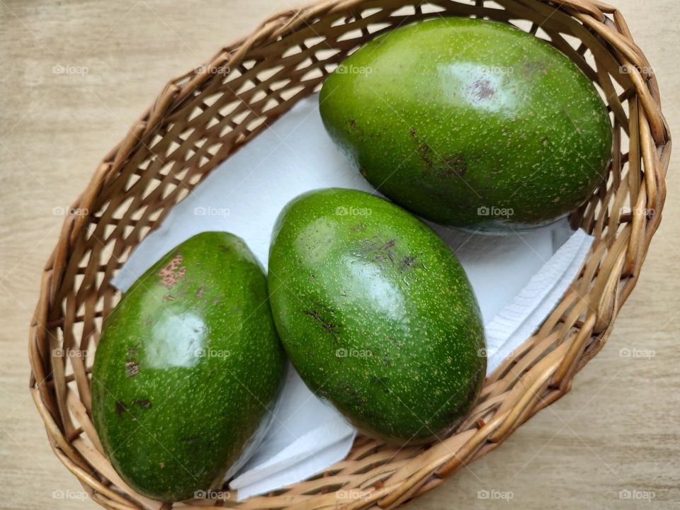 three green avocados in a wicker basket, waiting to ripen.