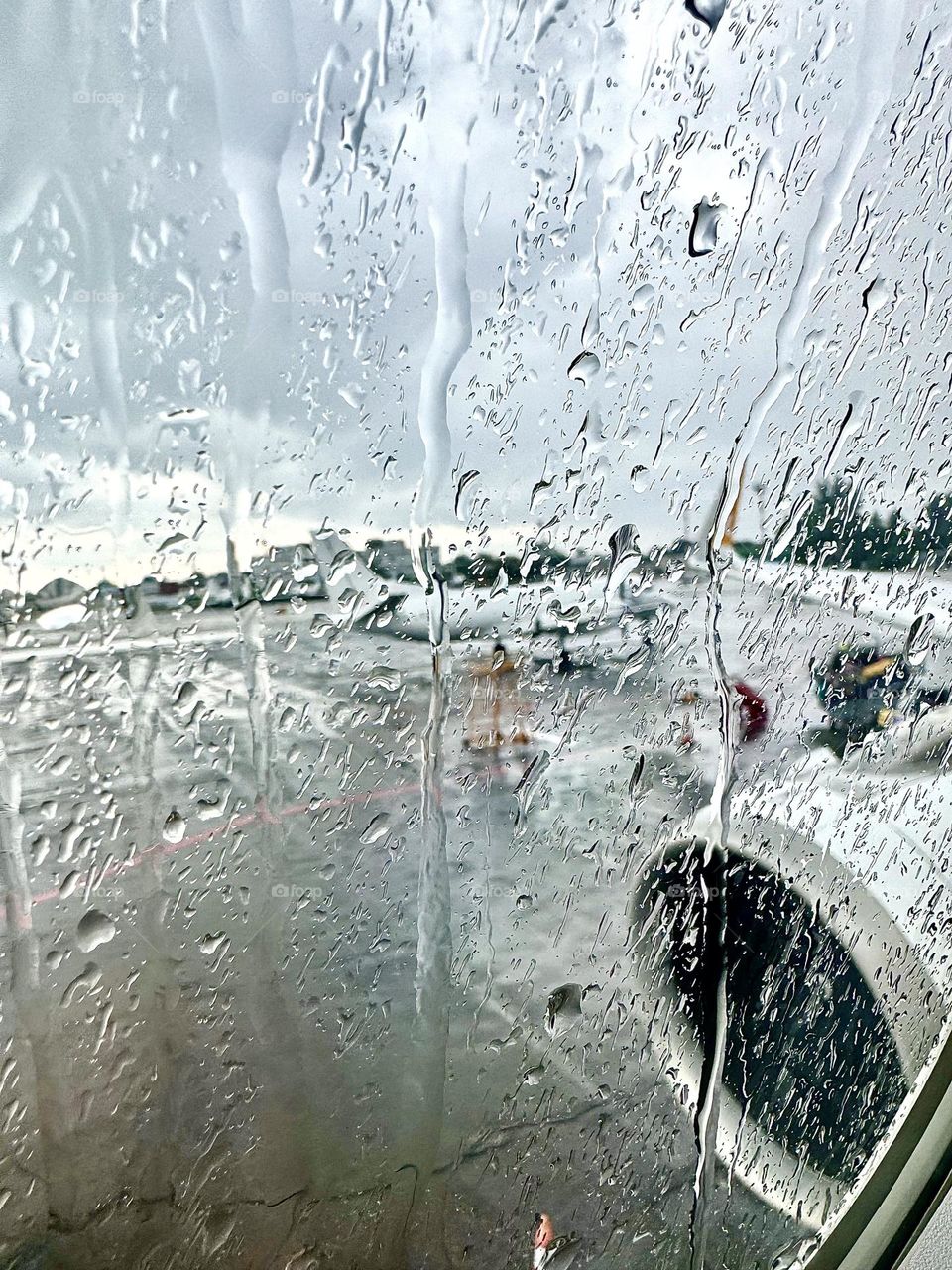 Outside the plane's window, rain can be seen streaming down the glass and several planes parked next to each other on the wet runway.