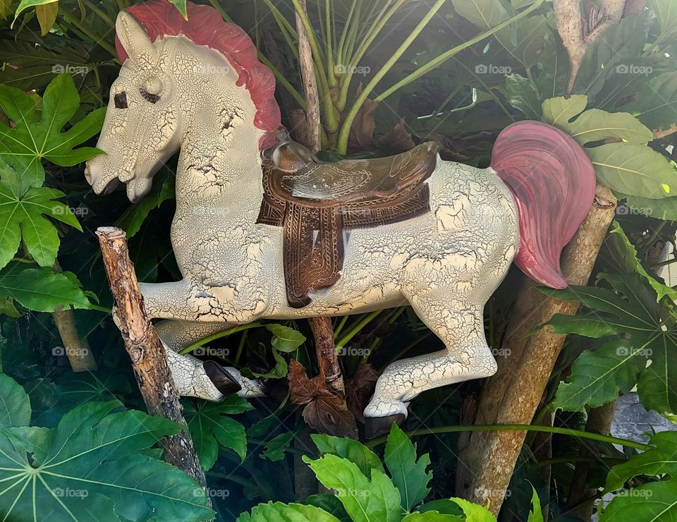 pink and white weathered wooden horse hidden amongst green leaves in front of a home in coastal Oregon