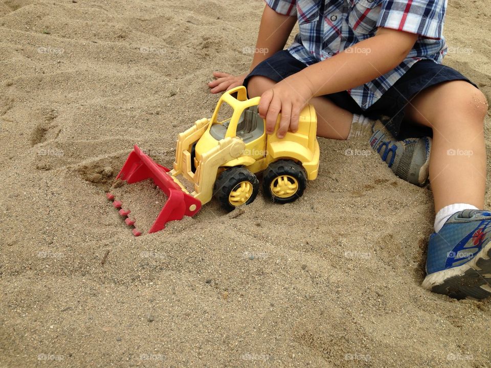 Child Playing With Toy Truck . A little boy plays with a yellow toy truck in the sand at the park.